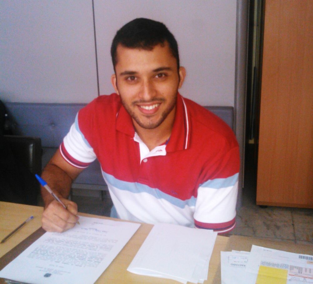 Filipe, de camisa polo listrada, sorrindo enquanto assina os documentos da posse no Colégio Pedro II